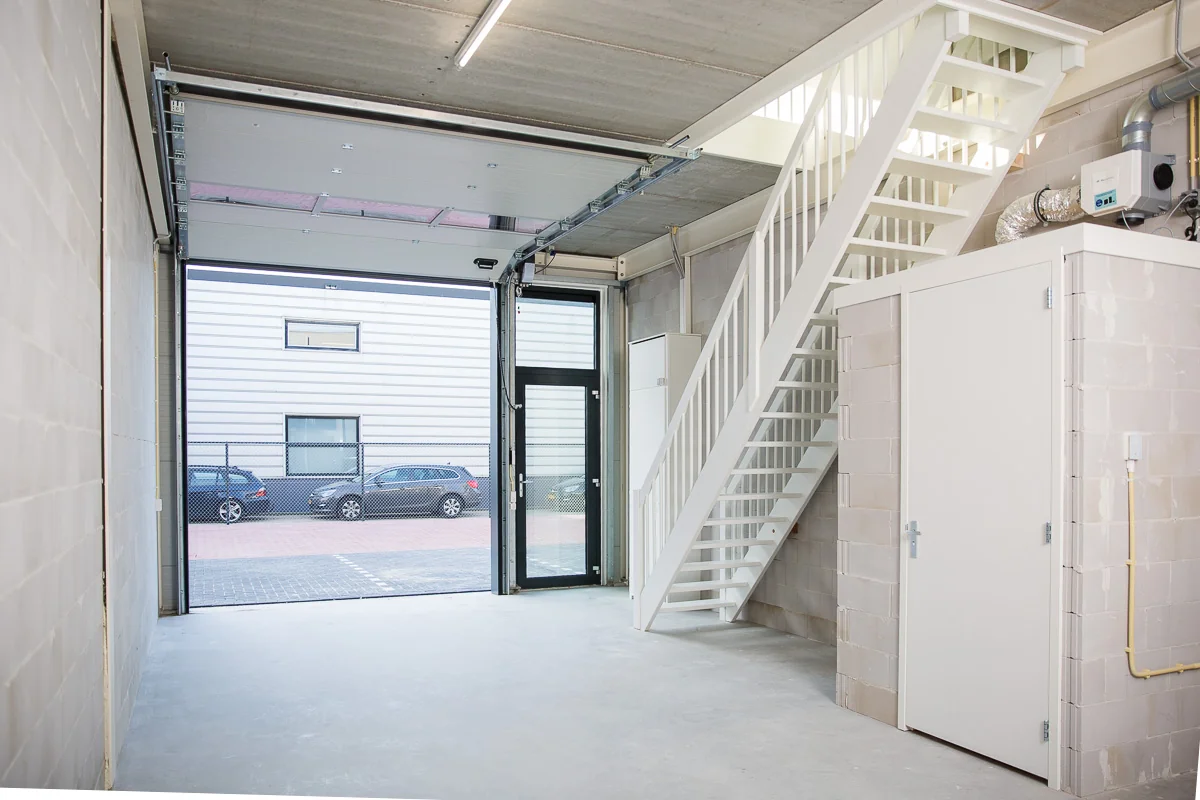 Interieur van een moderne bedrijfsruimte aan de Laan van S-Gravenmade met open garagedeur, trap en bergkast.